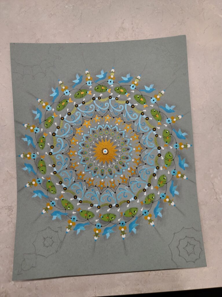 A partially completed mandala with teal, blue, green, yellow, and orange geometric shapes and marine life motifs radiating from the center.