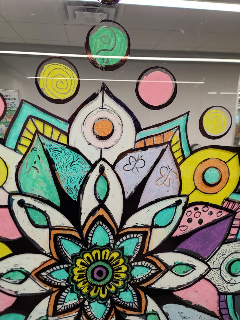  A close-up of a window mandala showing layered petals and colorful circular symbols, including a green yin-yang motif at the top.