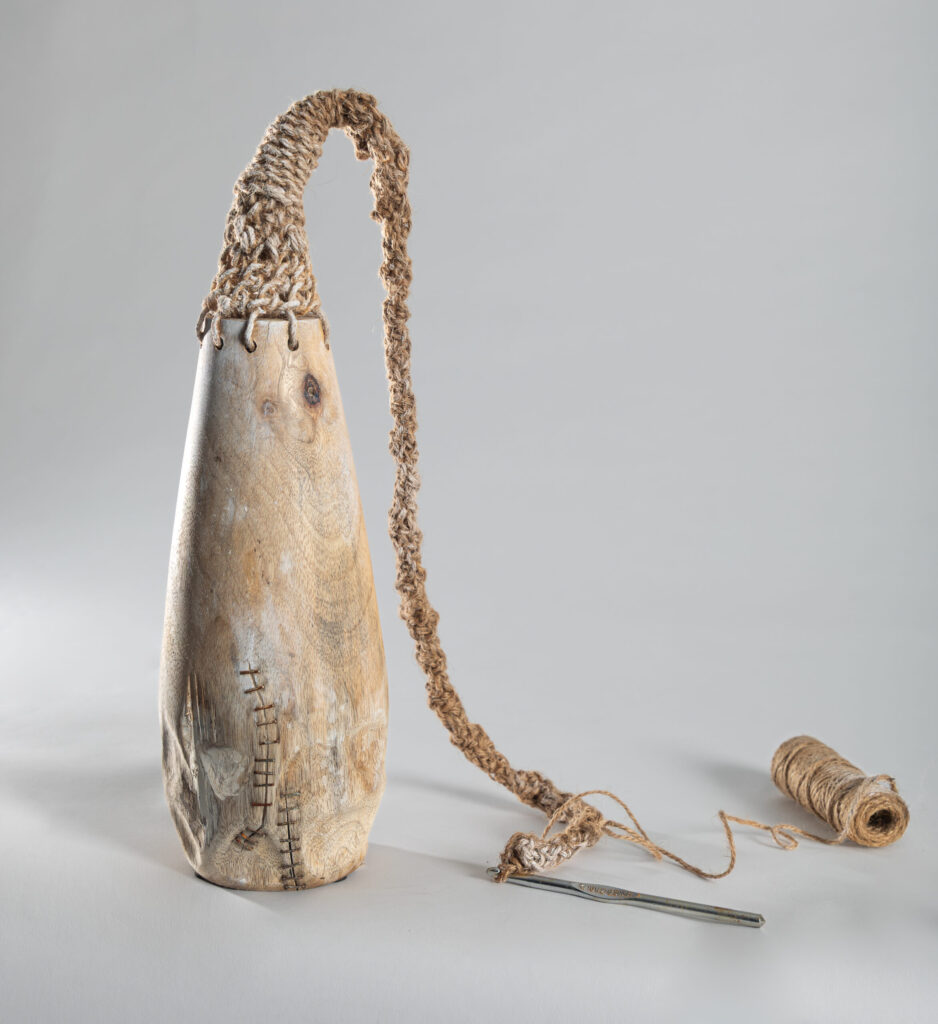 Bleached wooden vessel with crocheted jute extension collapsing under it's own weight, metal staples rusting through whitewash, crochet hook and spool in situ. Fiber Sculpture by Sarah A. Uys.